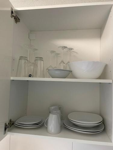 un armario blanco con platos, tazones y vasos en City Apartment Bad Säckingen mit Parkplatz en Bad Säckingen