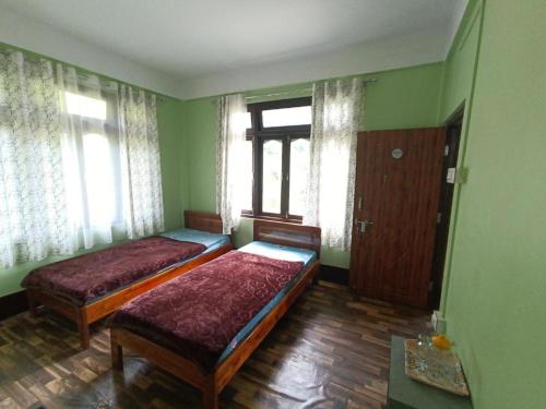 two beds in a room with green walls and windows at Mountain View Passaddhi Comfort Stay in Kalimpong