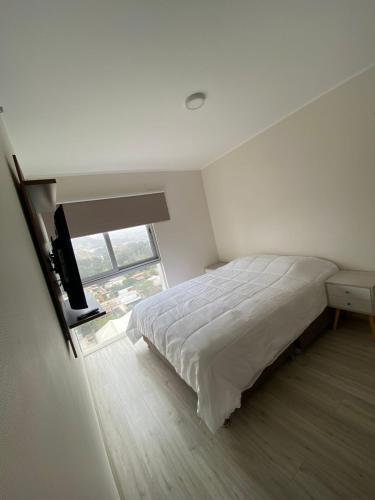 a white bedroom with a bed and a window at Dpto con hermosa vista al hipódromo de Monterrico in Lima