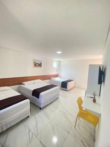 a bedroom with two beds and a yellow chair at Pousada O Sol De Maragogi in Maragogi