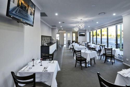 un restaurante con mesas y sillas blancas y TV en Astro Dish Motor Inn, en Parkes