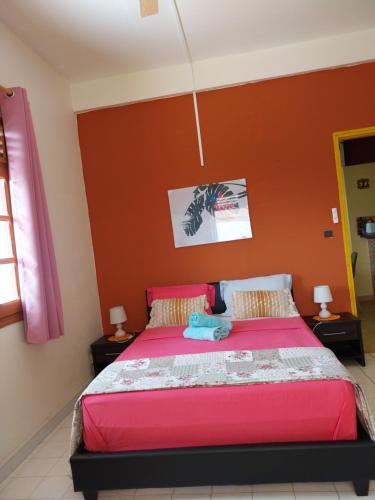 a bedroom with a bed with a red wall at BIENVENUE AU SOLEIL LEVANT assier entrée morne savon ,le lorrain in Le Lorrain