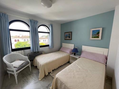 a bedroom with two beds and a chair and two windows at Casa de Playa in Estepona
