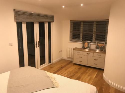 a bedroom with a bed and a dresser and windows at Redhill Lodge in Farnham