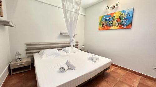 a bedroom with a white bed and a painting on the wall at La Pagerie, joli bas de villa avec piscine au calme à 5 minutes de la plage in Les Trois-Îlets