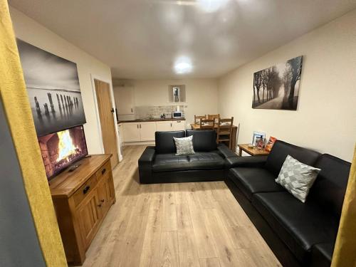 un salon avec un canapé noir et une télévision dans l'établissement Cosy & peaceful cottage in rural Northumberland, à Morpeth