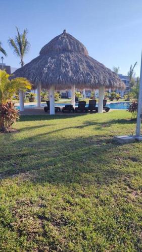 a straw hut with chairs and a swimming pool at Depto. frente al mar con Club de Playa in Acapulco