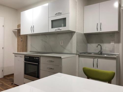 a kitchen with white cabinets and a green chair at Apartmani Kaić in Livno