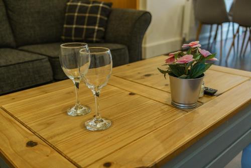 two wine glasses on a wooden table with a vase of flowers at Augusta lodge Moseley in Birmingham