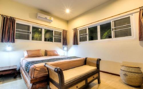 a bedroom with a bed and a bench and windows at Chaba Pool Villa in Nai Harn Beach