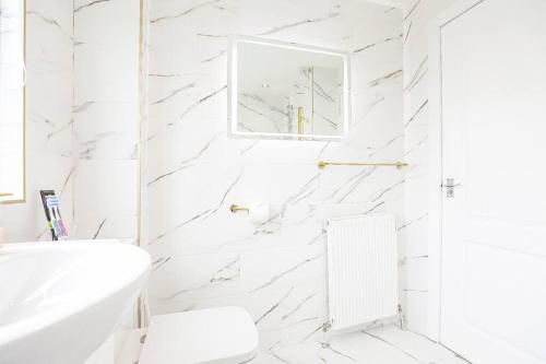 a white bathroom with white marble walls and a white tub at Doralan in Bishopbriggs