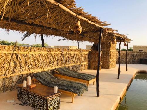 a group of chairs under a thatched roof next to a pool at Gazrashek Siwa Hot spring& trips Haven in Siwa