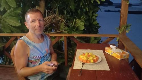Yohana Cottage في Tual: رجل يجلس على طاولة مع صحن من الفواكه