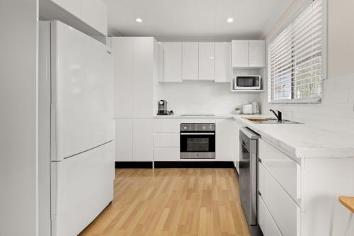 a white kitchen with white cabinets and a wooden floor at Corinya Cottage By Experience Jervis Bay in Worrowing Heights