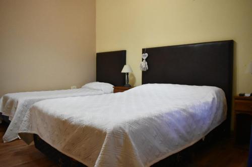 two beds in a hotel room with white sheets at El Colonial in Colón