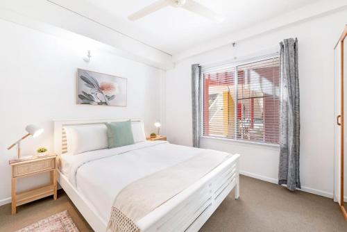 a white bedroom with a large bed and a window at Cullen Bay Calm - Tropical Poolside Living in Larrakeyah