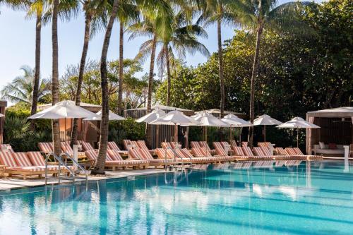 a pool with chairs and umbrellas and palm trees at W South Beach in Miami Beach