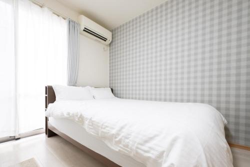 a bedroom with a white bed and a tiled wall at 駅近徒歩3分。生活に便利なアパート。長期滞在にもオススメ in Daitō