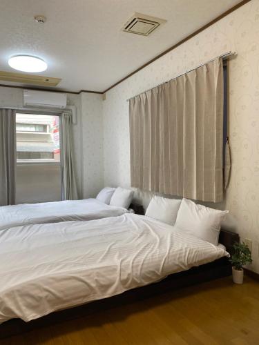 una camera con due letti con lenzuola bianche e una finestra di Guest House Flora Otemachi/フローラ大手町 a Hiroshima