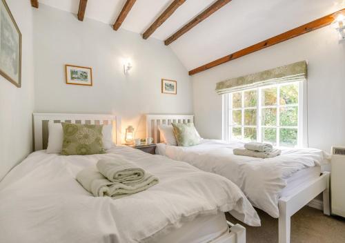 two beds in a room with white walls and a window at Dowr Penty in Helford