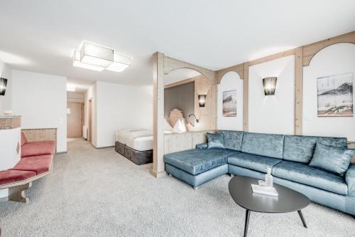 a living room with a blue couch and a bed at SKI - GOLF - WELLNESS Hotel Riml in Hochgurgl