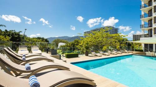 a pool with lounge chairs next to a building at Pacific Hotel Cairns in Cairns