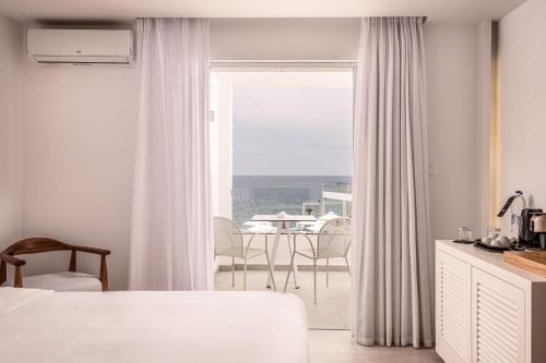 een witte kamer met een raam en een tafel met stoelen bij Kantouni Beach Boutique Hotel in Panormos Kalymnos