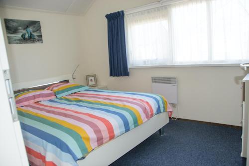 een slaapkamer met een bed met een kleurrijk gestreepte deken bij Fries Vakantiehuis, grote tuin, nabij het Pikmeer in Grou