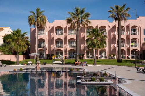 een groot roze gebouw met palmbomen voor een zwembad bij Vila Gale Collection Praia in Albufeira
