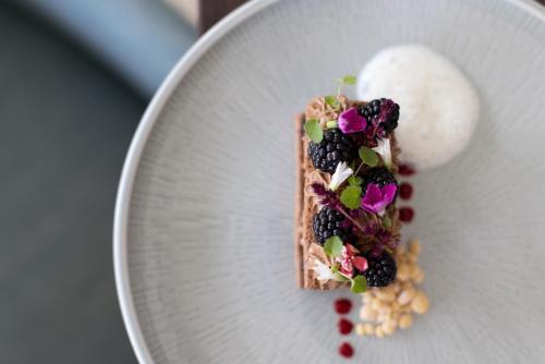 a piece of cake with blackberries and flowers on a plate at Hilburger Hotel in Schenna
