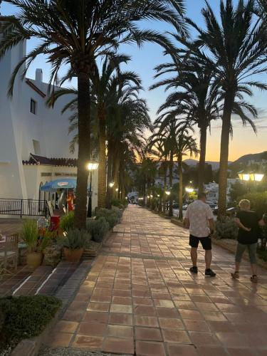 two people walking down a sidewalk with palm trees at Lovely studio Nerja ground floor in Nerja