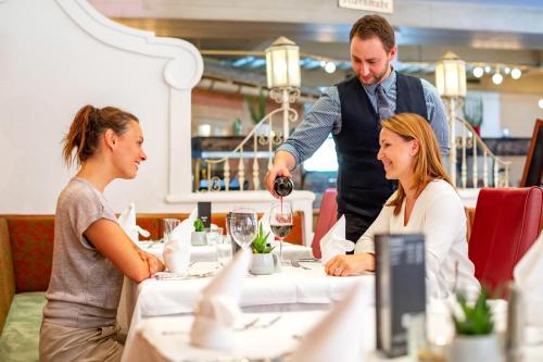 a man pouring a woman a glass of wine at a table at JUFA Alpenhotel Saalbach-Jokercard im Sommer inklusive in Saalbach Hinterglemm