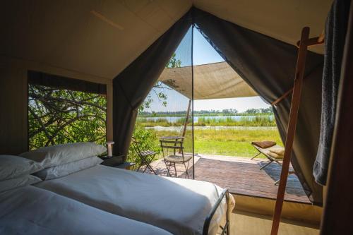 a tent with a bed and a deck with a chair at Cha Cha Metsi in Maun