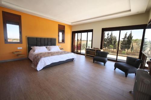 a bedroom with a bed and two chairs and windows at Villa Tizra - Guest house in AÃ¯n el Ksob