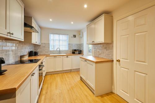 a kitchen with white cabinets and a wooden floor at Host & Stay - Sandstone Cottage in Skelton