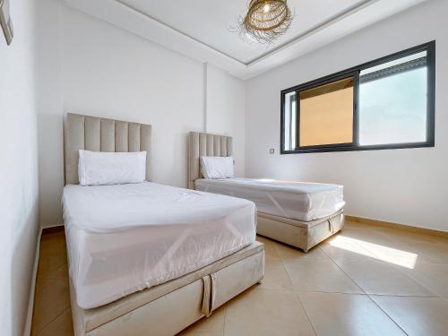 two beds in a white room with a window at La Perle Taghazout apparts 2-3px in Taghazout