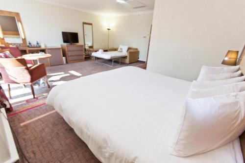 a bedroom with a large white bed and a living room at Hilton London Olympia in London