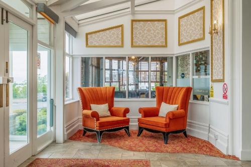 two orange chairs in a hallway with windows at Muthu Westcliff Hotel (Near London Southend Airport) in Southend-on-Sea