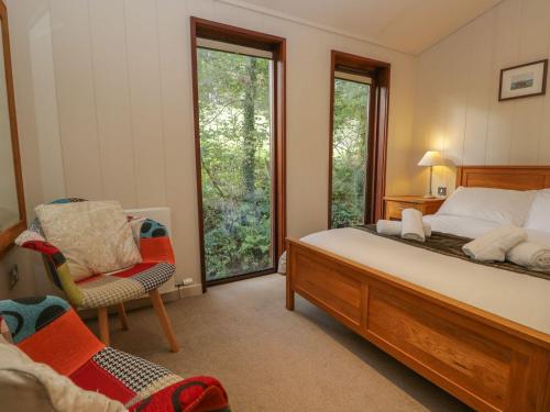a bedroom with a bed and a chair and windows at Leafy Nook Lodge in Ambleside