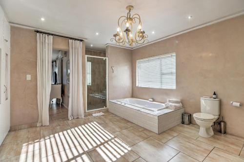 ein Badezimmer mit einer Badewanne, einem WC und einem Kronleuchter in der Unterkunft Thyme Wellness Spa and Guesthouse in Kapstadt