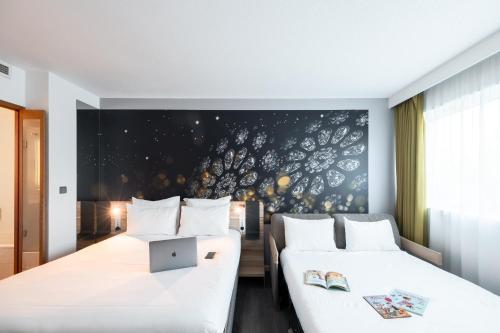two beds in a hotel room with a laptop on a wall at Novotel Chartres in Chartres