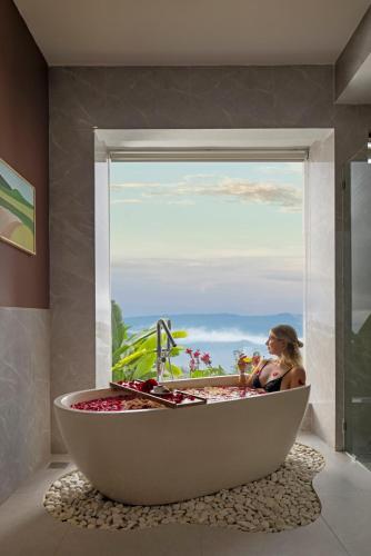 a woman sitting in a bath tub in front of a window at Munduk Tentrem Resort in Munduk