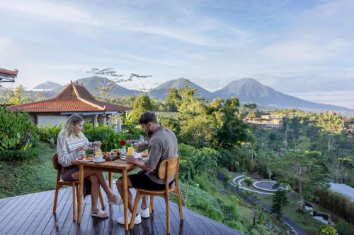 a man and woman sitting at a table on a deck at Munduk Tentrem Resort in Munduk