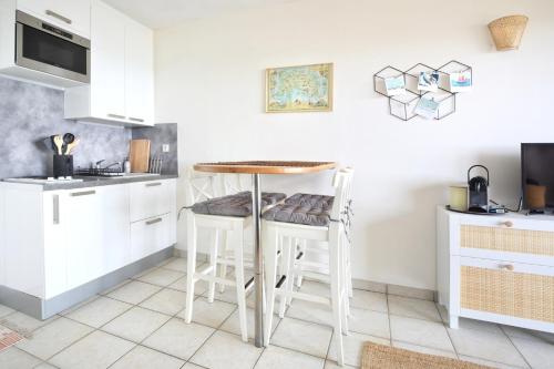 - une cuisine avec tabourets blancs et table dans l'établissement Le balcon de Jersey - face à la mer, à Saint-Jean-de-la-Rivière