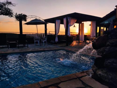 a swimming pool with a fountain in front of a sunset at Pousada Palavras Novas in Lavras Novas
