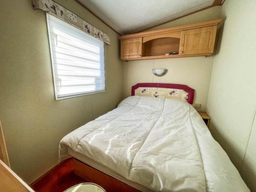 Cama pequeña en habitación pequeña con ventana en Wonderful 8 Berth Caravan At Seawick Holiday Park In Clacton-on-sea Ref 27077r, en Clacton-on-Sea