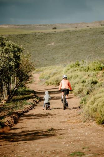 a man riding a bike down a dirt road with a child at Breathe Accommodation in Oudtshoorn