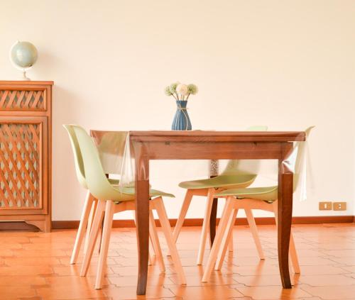 una mesa de madera con sillas verdes y un jarrón de flores en "La Villa dei Nonni" appartamento, en Bérgamo