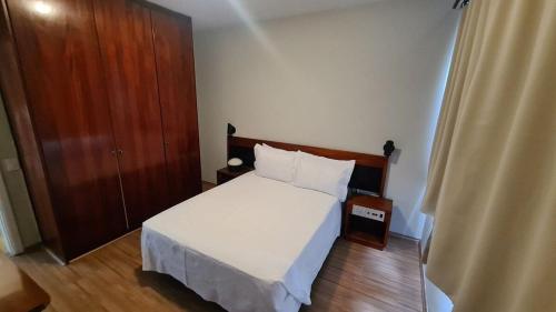 1 dormitorio con cama blanca y armario de madera en TrevizZo no Hotel Astran en São Bernardo do Campo