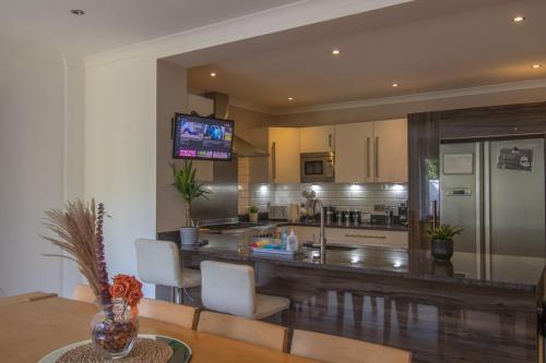 a kitchen with a counter with white chairs and a television at 6 Bedroom Holiday Home with Hot Tub & Garden in Luton